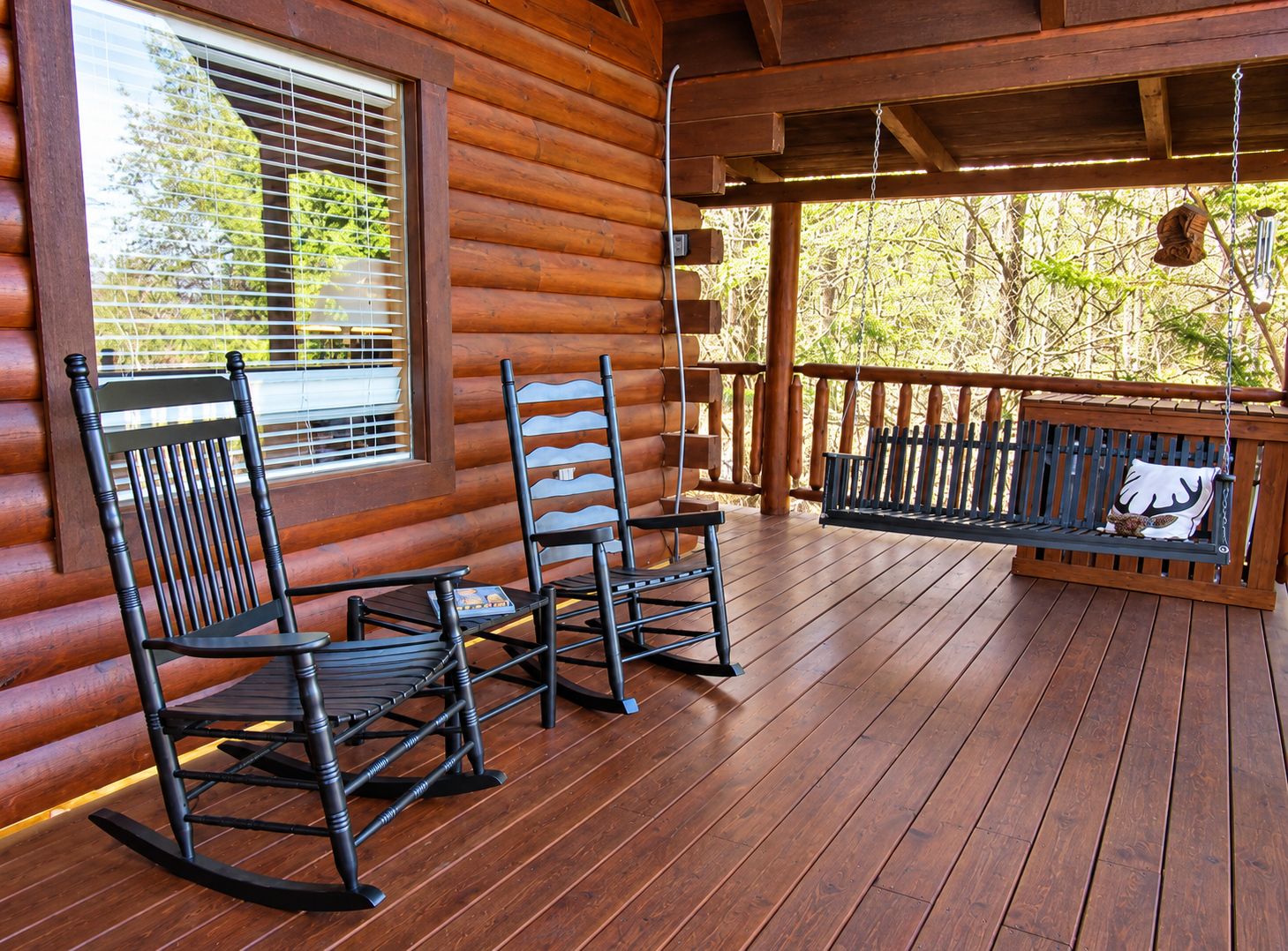 Una terraza de madera con mecedoras y un banco, con vista a un paisaje natural.