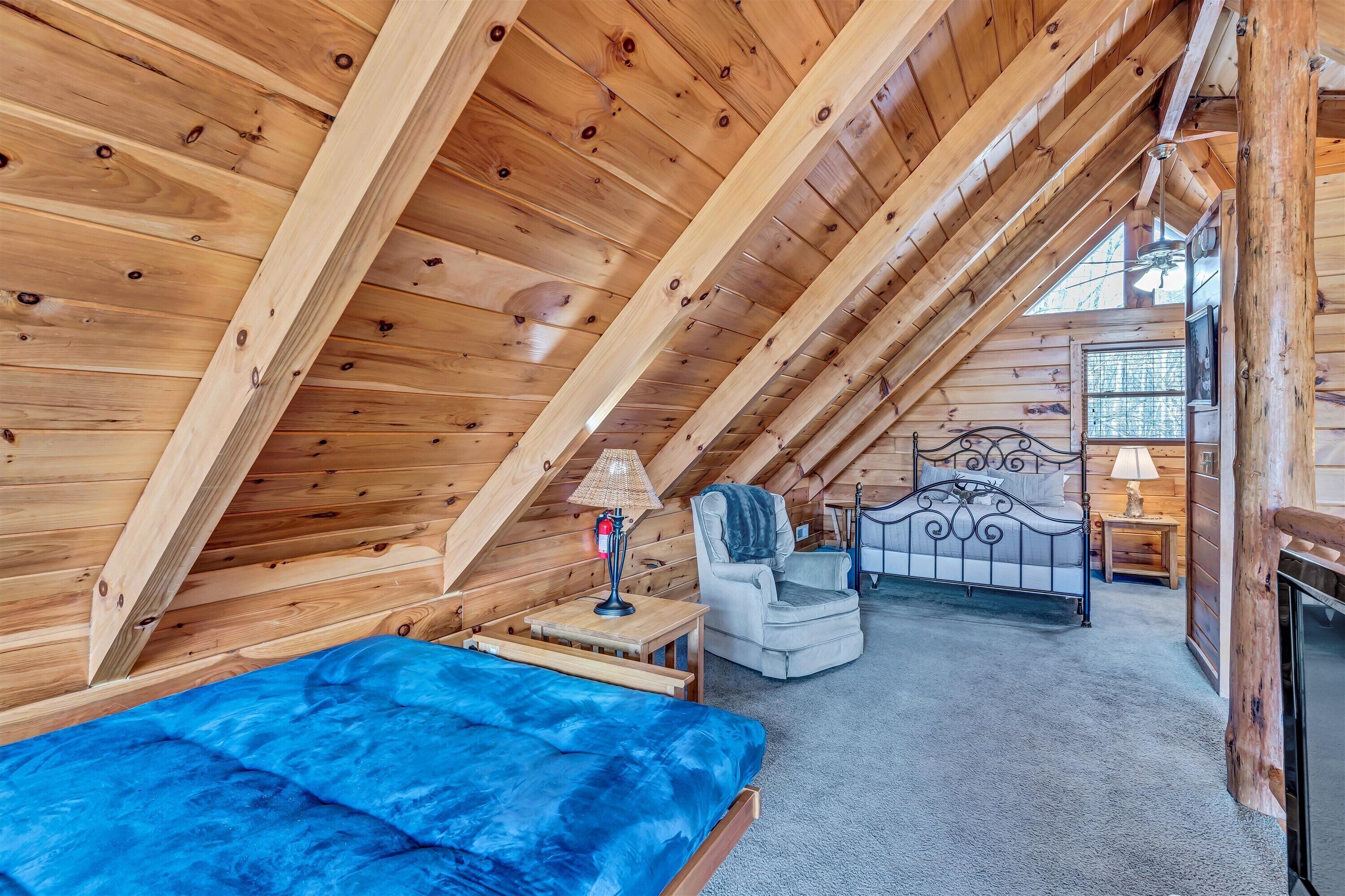 A cozy attic bedroom with a bed, chair, and a small table with a lamp.