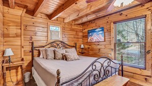 Un dormitorio de cabaña de madera con cama, mesitas de noche y una ventana con persianas.