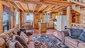 Interior acogedor de una cabaña con detalles de madera, un sofá, un tapete estampado y una zona de cocina.