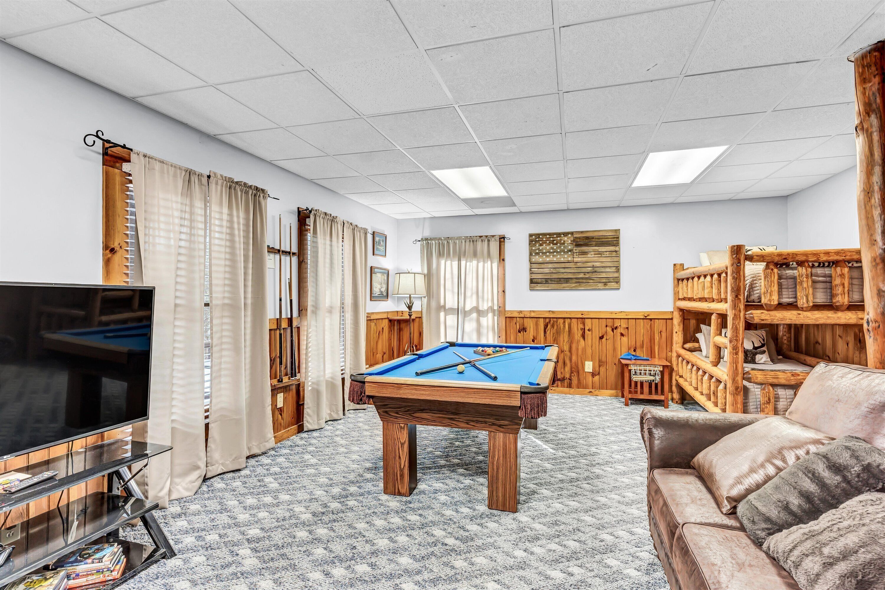 A room with a pool table, a television, a sofa, and a wooden bookshelf.