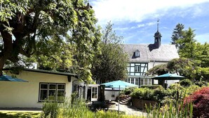 Um edifício tradicional em estilo Tudor com uma torre imponente, rodeado por jardins exuberantes e um lago com vitórias-regias.