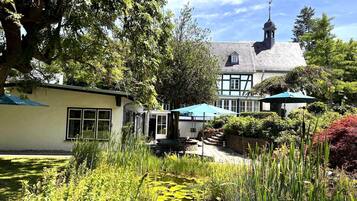 A traditional Tudor-style building with a prominent tower, surrounded by lush gardens and a pond with lily pads.