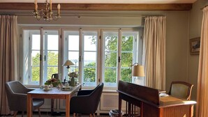 Um quarto com uma mesa de madeira, duas cadeiras, uma escrivaninha e uma janela com cortinas.