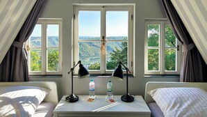 Ein Zimmer mit zwei Betten, einem Tisch mit zwei Lampen und Blick auf eine Landschaft durch große Fenster.
