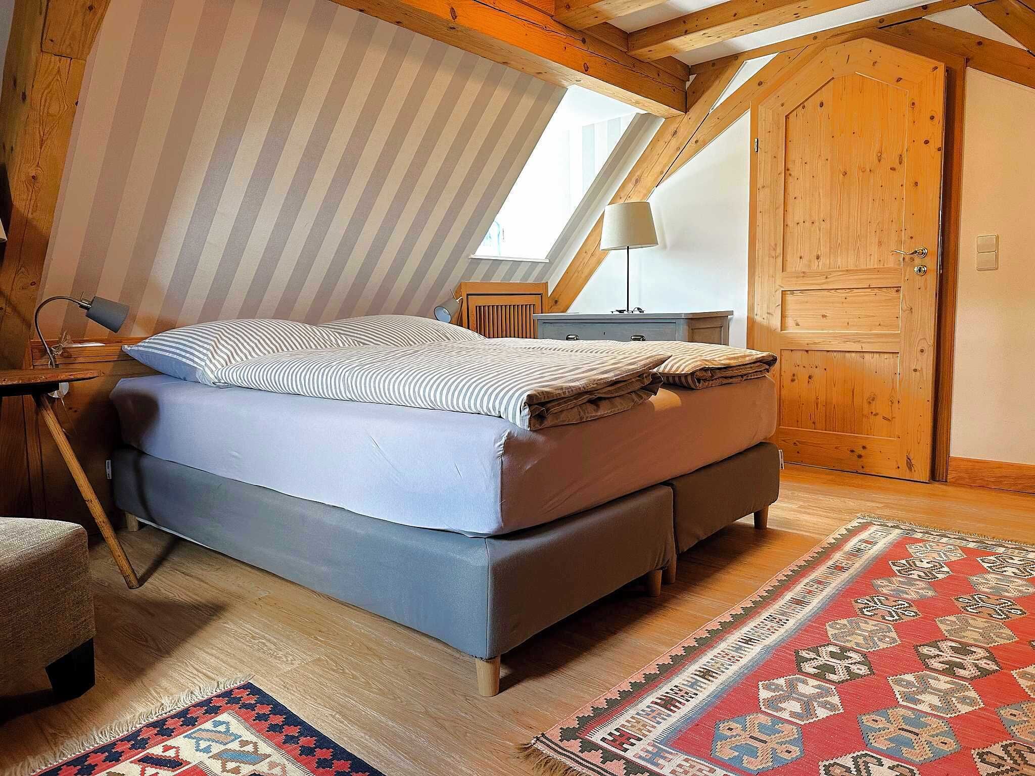 A bedroom with a loft bed, a wooden wardrobe, a small bedside table, and a lamp.