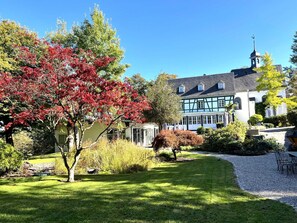 A traditional building with a prominent tower, surrounded by a well-maintained garden with various trees and shrubs. - Holiday Home Mister Stringer in Altes Forsthaus Boppard (Boppard)