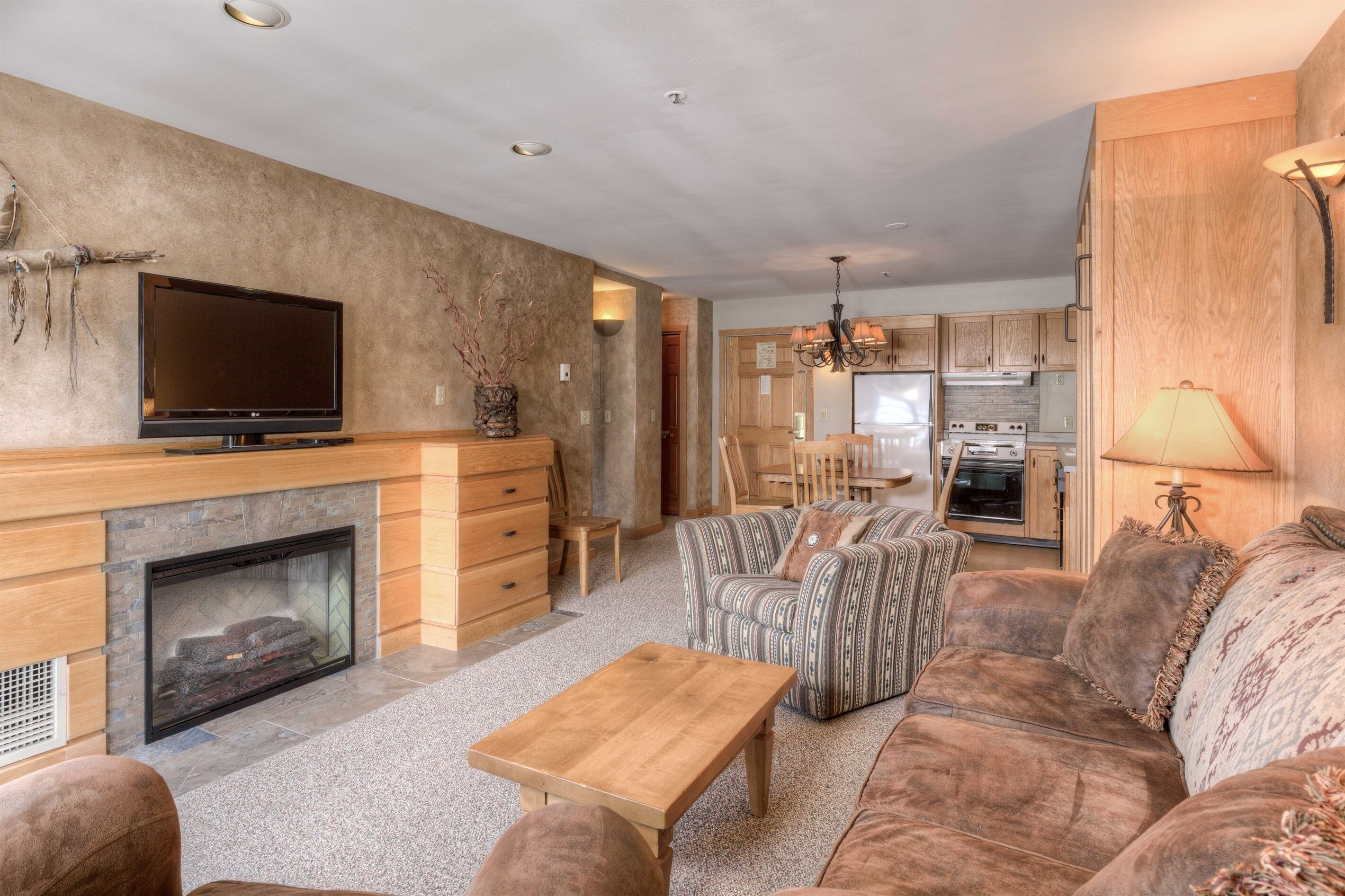 A modern living room with a fireplace, a television, and a dining area with wooden cabinets and a chandelier.