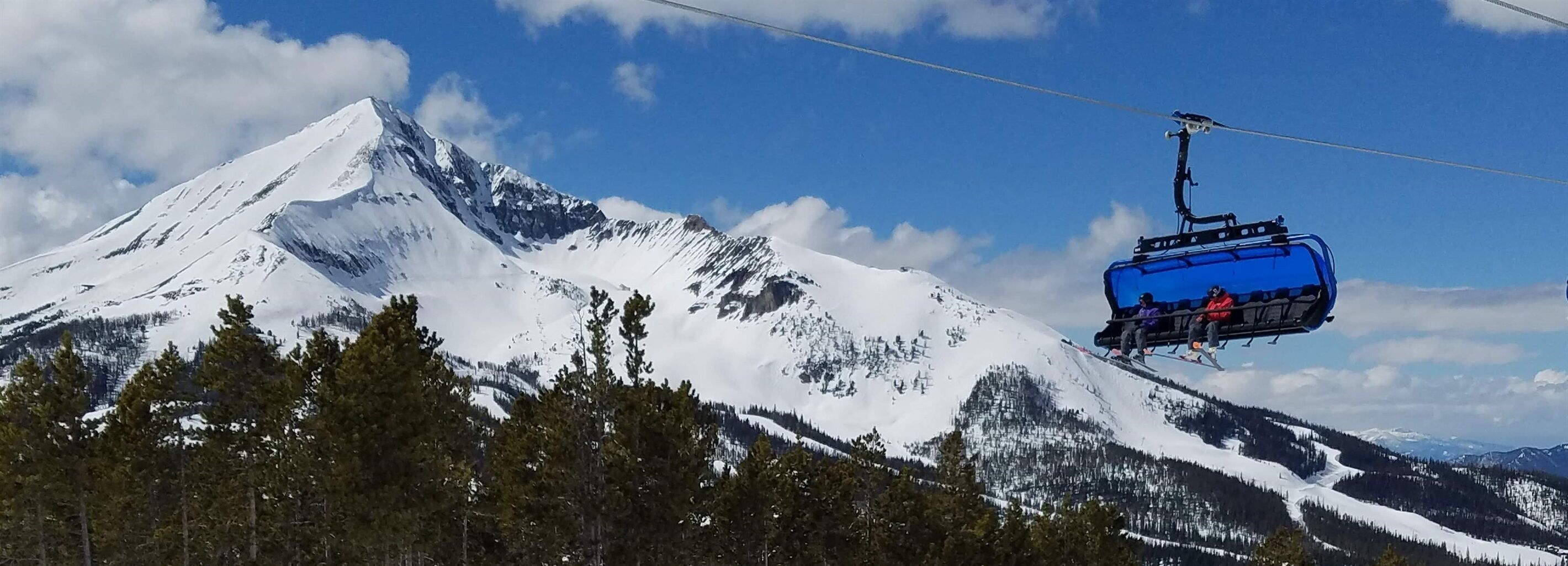 Eine Seilbahn fährt einen schneebedeckten Berg hinauf, bewölkter Himmel.