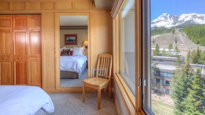 Ein Schlafzimmer mit einem Holzschrank, einem Bett, einem Stuhl und einem großen Fenster mit Blick auf die Berge.