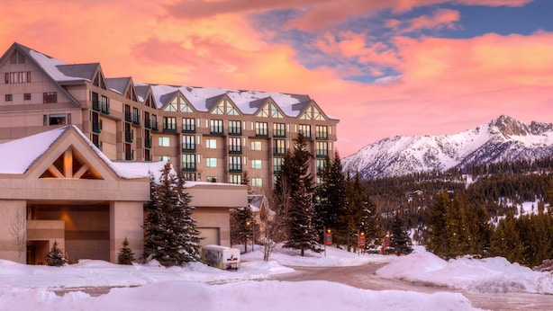 Ein mehrstöckiges Hotel mit verschneitem Dach und einer Bergkulisse.