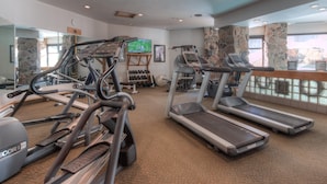 Ein Fitnessstudio mit Laufbändern, Crosstrainern und einem Fernsehbildschirm.