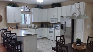 A kitchen with white cabinets, a central island, and a dining area with wooden chairs and a table. - 2 BEDROOM CONDO IN THE HEART of OSAGE BEACH at the LAKE!!! (Osage Beach)