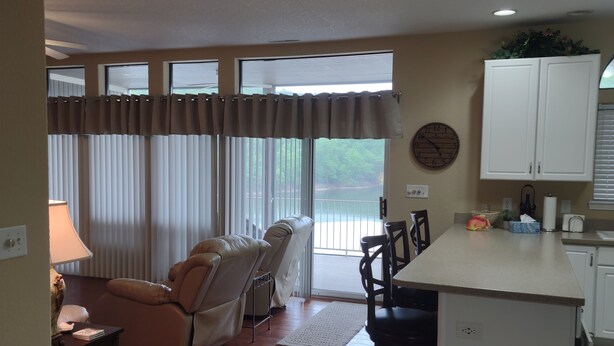 A spacious living area with a sofa, chairs, a dining table, and a kitchen area with cabinets and a clock on the wall. - 2 BEDROOM CONDO IN THE HEART of OSAGE BEACH at the LAKE!!! (Osage Beach)