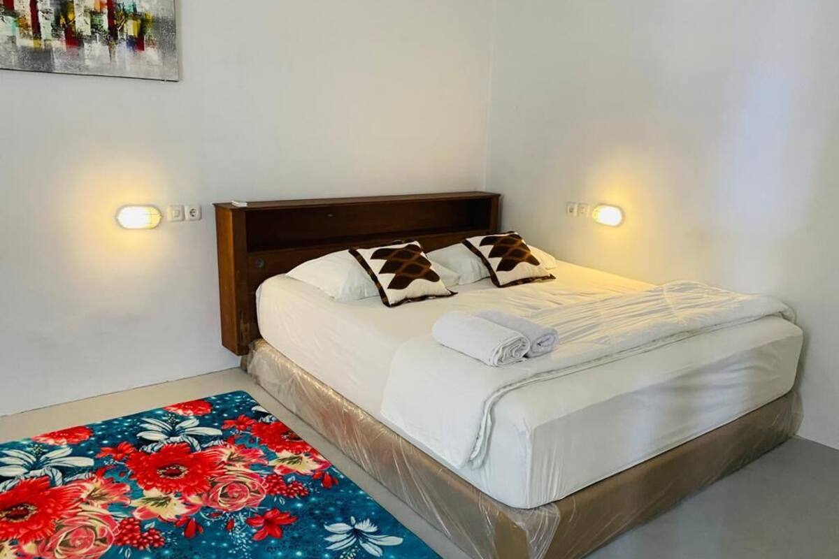 A neatly made bed with white linens and two decorative pillows, a wooden headboard, and two wall-mounted light fixtures.