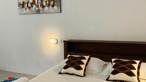 A neatly made bed with white linens and patterned pillows, a wall-mounted abstract painting, and a bedside lamp. - Komodo Indah Hotel (Labuan Bajo)