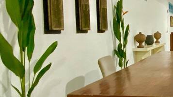 Un espace repas avec une longue table en bois, des plantes en pot et des objets décoratifs fixés au mur.