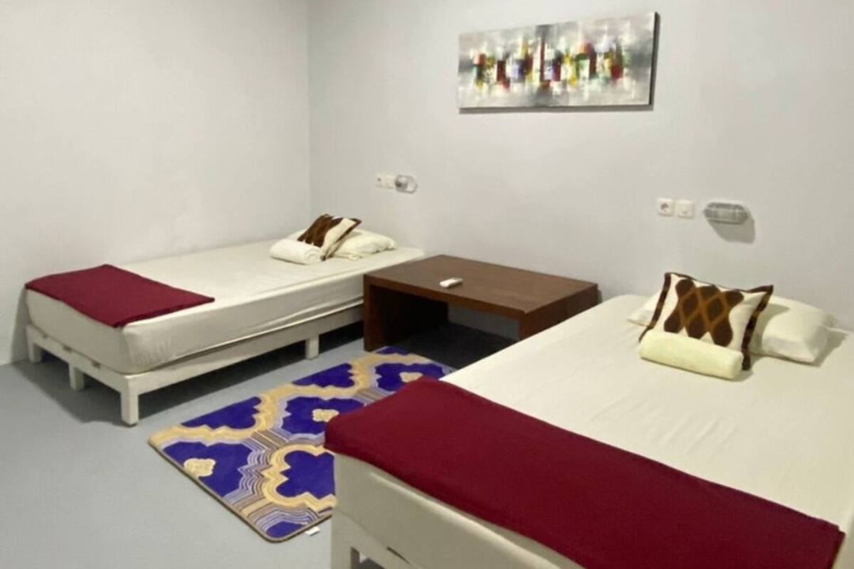 A hotel room with two single beds, a small table, and a rug.