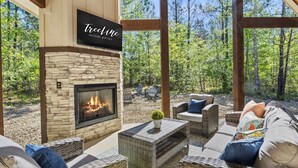 A cozy outdoor seating area with wicker furniture, a stone fireplace, and a sign reading "TreeLine Vacation Retreatals."