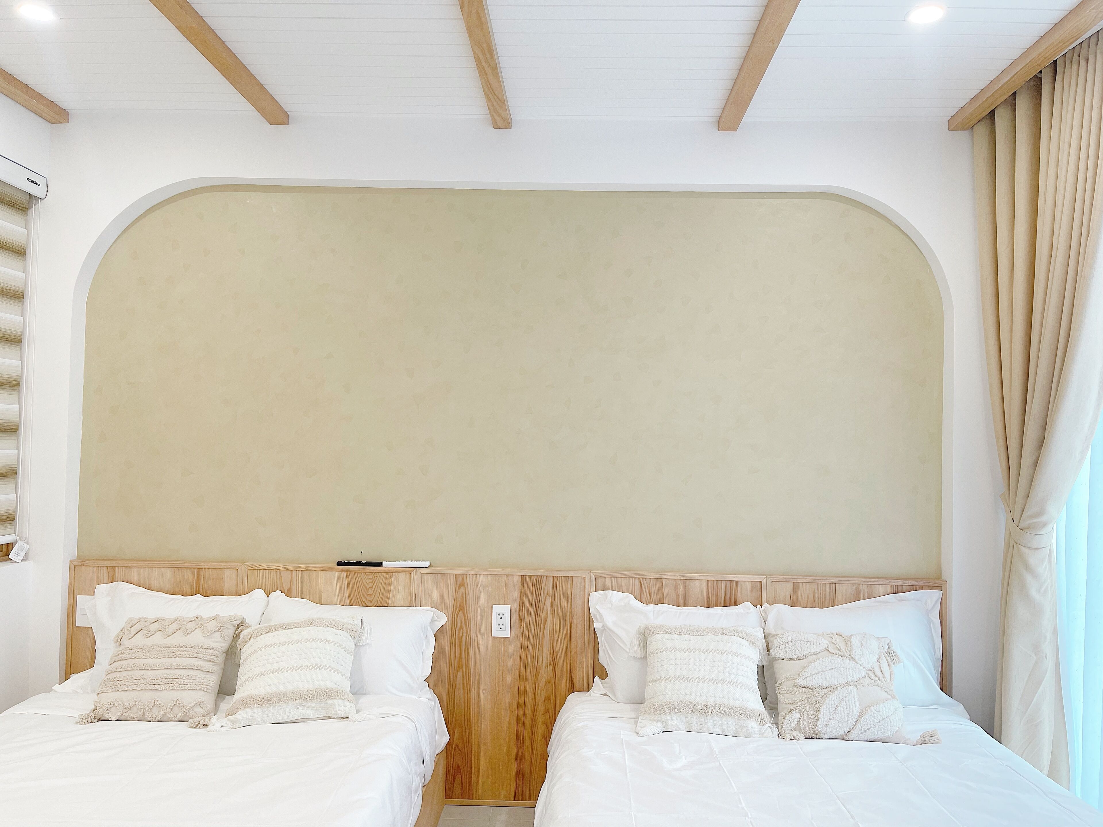 A hotel room with two beds, wooden headboards, and a large window with curtains.