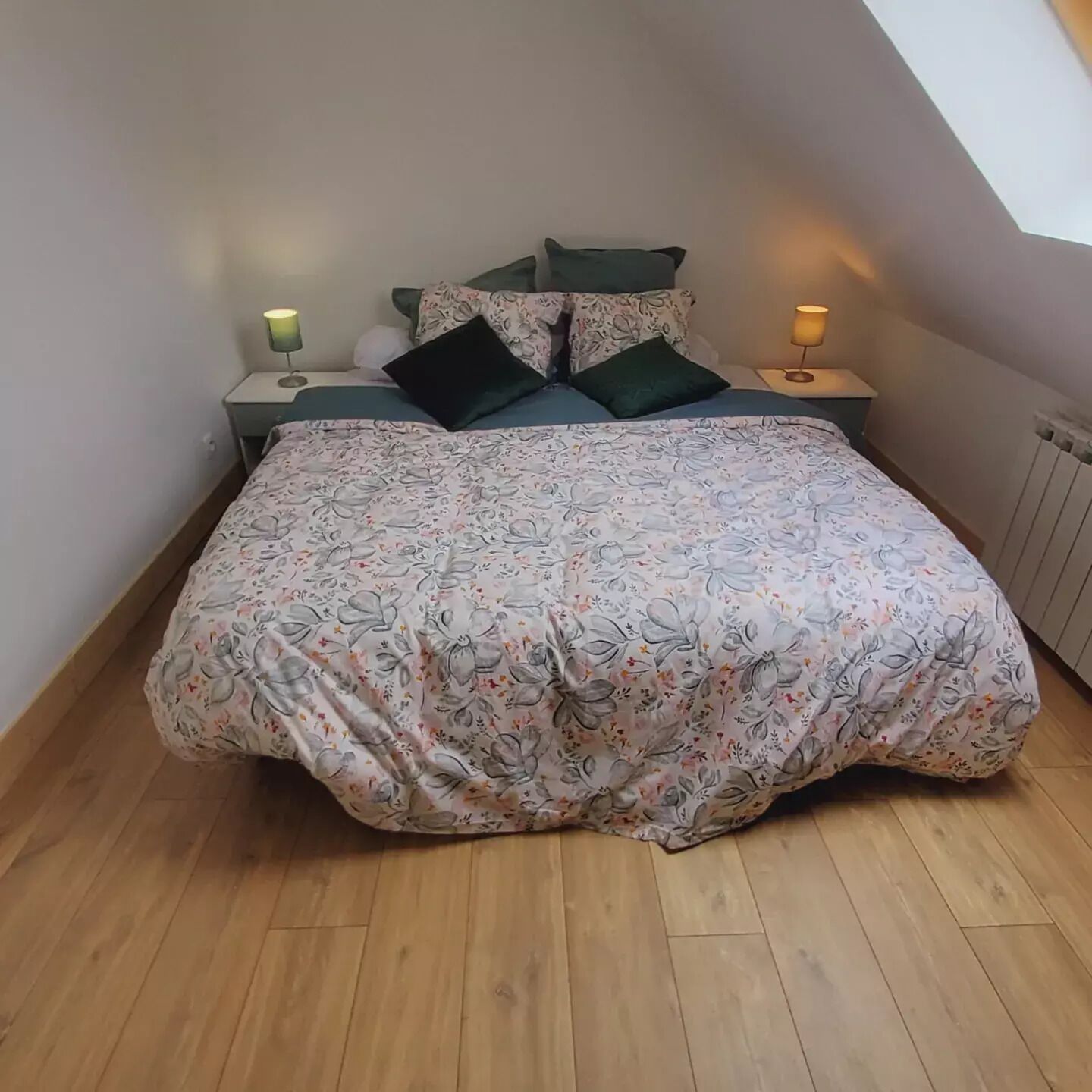Une chambre avec un grand lit, deux tables de chevet avec des lampes et un plafond en pente.