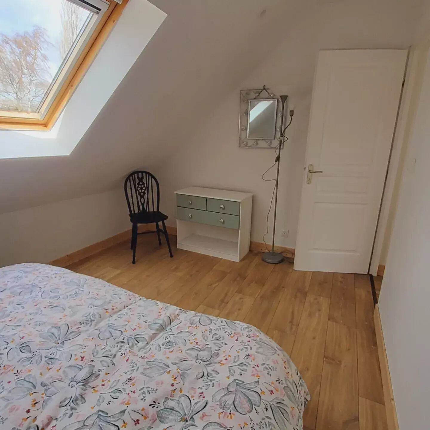 Un dormitorio con cama, una silla, un aparador, un espejo y una puerta.
