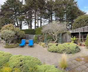 Een tuin met een houten constructie, een grindpad en blauwe lounge stoelen.