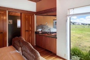Een slaapkamer met een bed, een rieten bank, een houten garderobe en een raam met uitzicht op een grasveld.