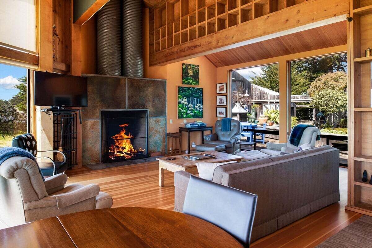 A modern living room with a fireplace, comfortable seating, and large windows offering a view of the outdoors.