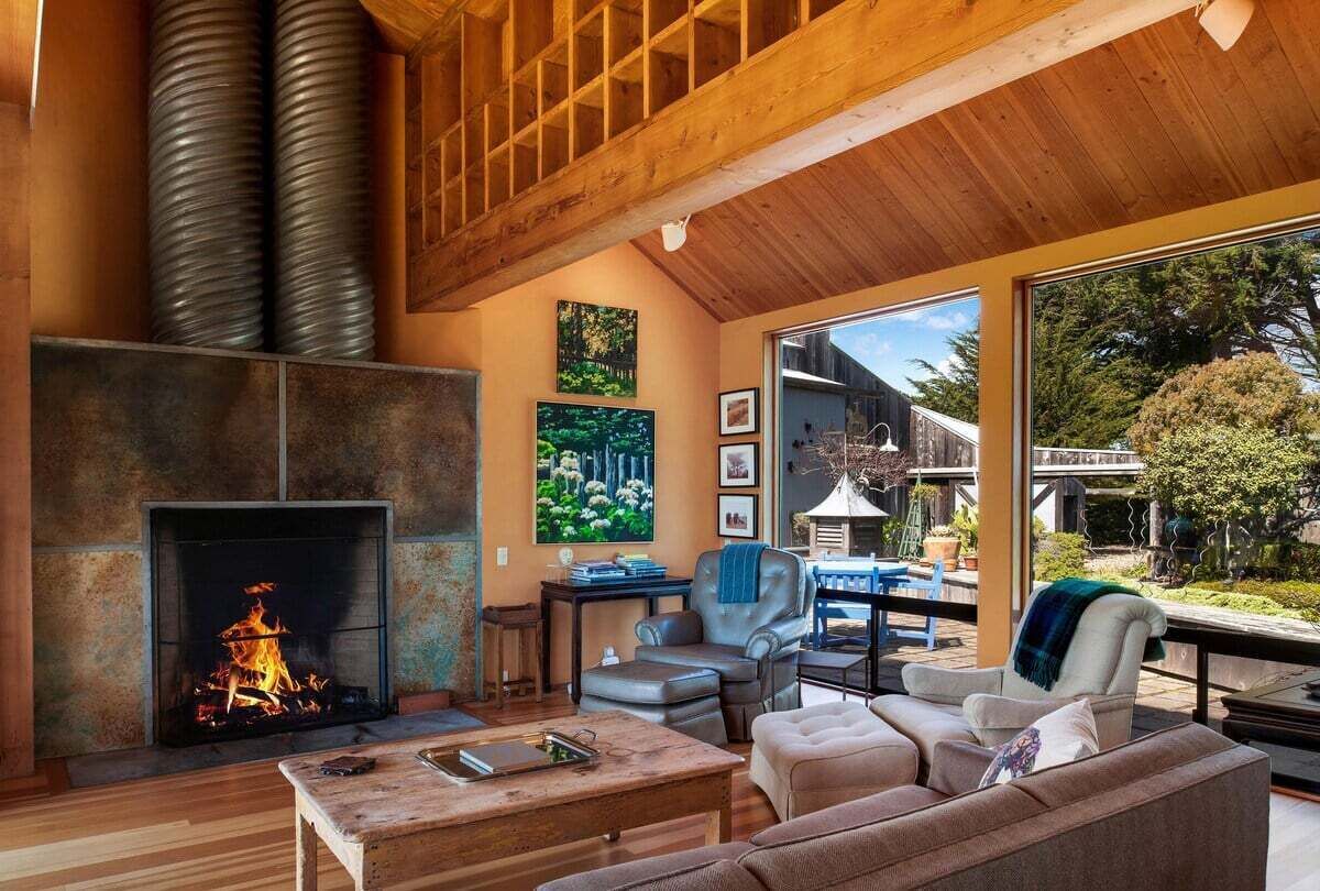 A cozy living room with a fireplace, leather furniture, and large windows offering a view of the outdoors.