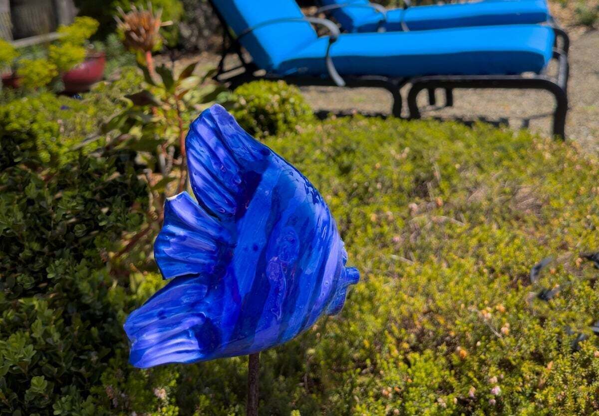 A blue glass sculpture in a garden with a pool and lounge chairs in the background.