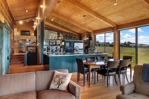A spacious kitchen with a central island, wooden ceiling, and large windows offering a view of the outdoors.