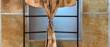A curtain on a metal stand with a textured wall in the background.