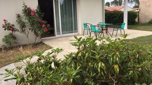 Ein Haus mit Terrasse, einer Schiebetür und einem kleinen Garten mit Büschen und einer Rosenpflanze.