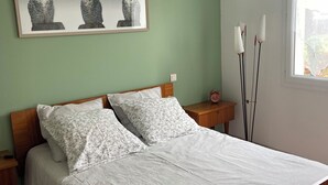 Ein Schlafzimmer mit einem Bett, einem Holzkopfstück, zwei Nachttischen, einem Bilderrahmen mit einer Eule, einem Fenster und einer Pendelleuchte.