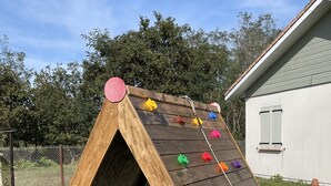 Eine hölzerne Kletterwand mit bunten Griffen, eingebettet in eine grüne Rasenfläche, mit einem Haus im Hintergrund.