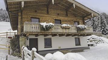 Ein traditionelles Holzhäuschen mit Balkon, vor einer verschneiten Landschaft gelegen.