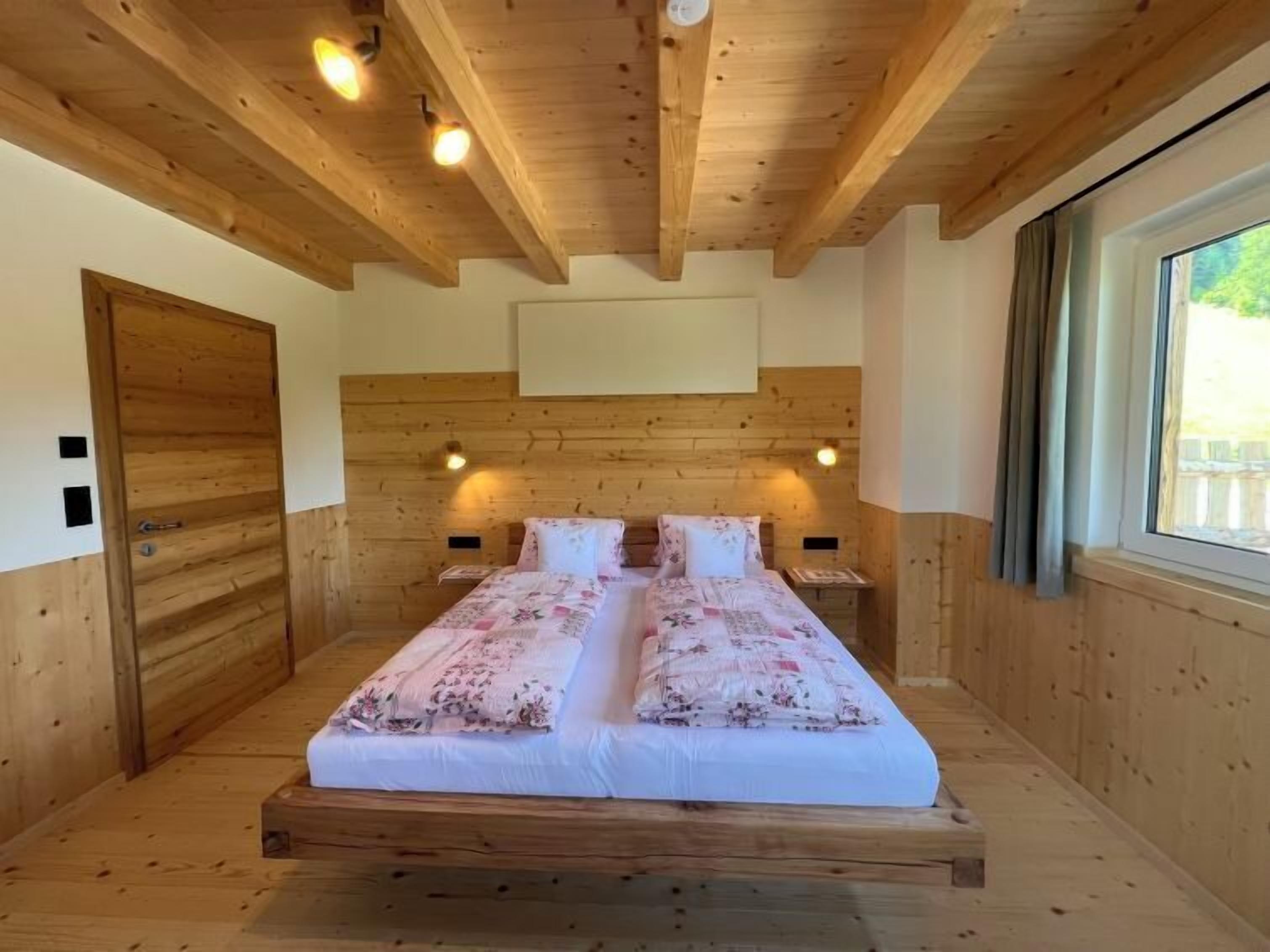 Ein Schlafzimmer mit Holzvertäfelung, einem großen Bett, zwei Nachttischen und einem Fenster mit Vorhängen.