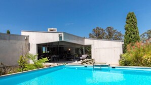 Ein modernes Haus mit Schwimmbad, Sitzgelegenheiten im Freien und einem Garten.
