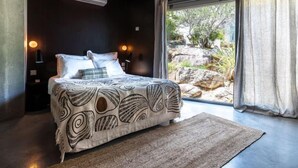 Ein Schlafzimmer mit einem großen Bett, zwei Nachttischlampen, einem Fenster mit Vorhängen und Blick ins Freie.