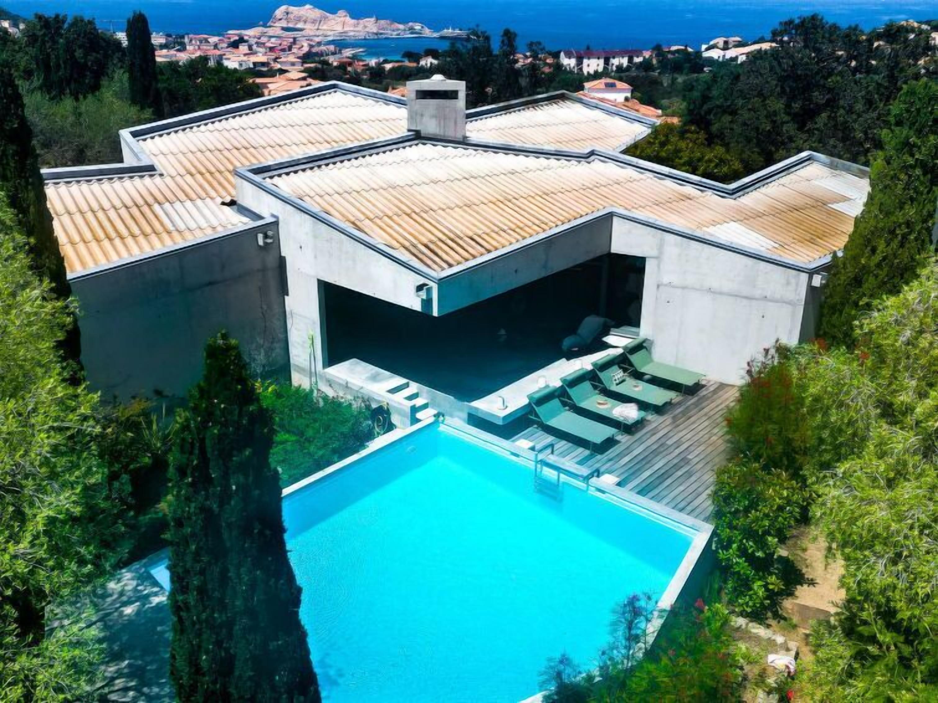 A modern house with a swimming pool, outdoor seating, and a view of the sea.