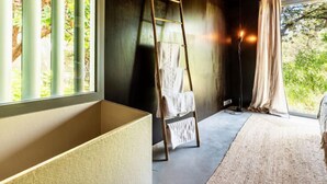 Ein Schlafzimmer mit großem Fenster, einer Hockerleiter, einem Nachttisch und einer Stehlampe.