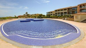 Una grande piscina circolare con decorazioni a mosaico blu, circondata da un solarium in pietra.