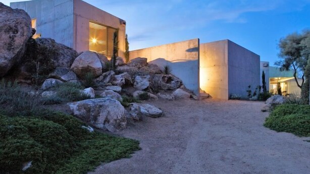 Un bâtiment moderne, doté d’une façade en béton et d’un chemin de terre menant à l’entrée.