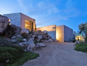 Un bâtiment moderne, doté d’une façade en béton et d’un chemin de terre menant à l’entrée.