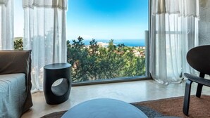 Un salon moderne doté d’une grande fenêtre offrant une vue panoramique sur la mer et la verdure.
