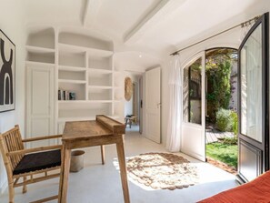 Um interior moderno com uma mesa e cadeiras de madeira, uma estante branca e vista para um jardim através de uma porta de vidro.