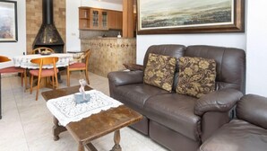 A living room with a brown leather sofa, a small wooden table, and a dining area with a white tablecloth.