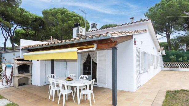 A white villa with a tiled patio, outdoor seating, and a pizza oven.