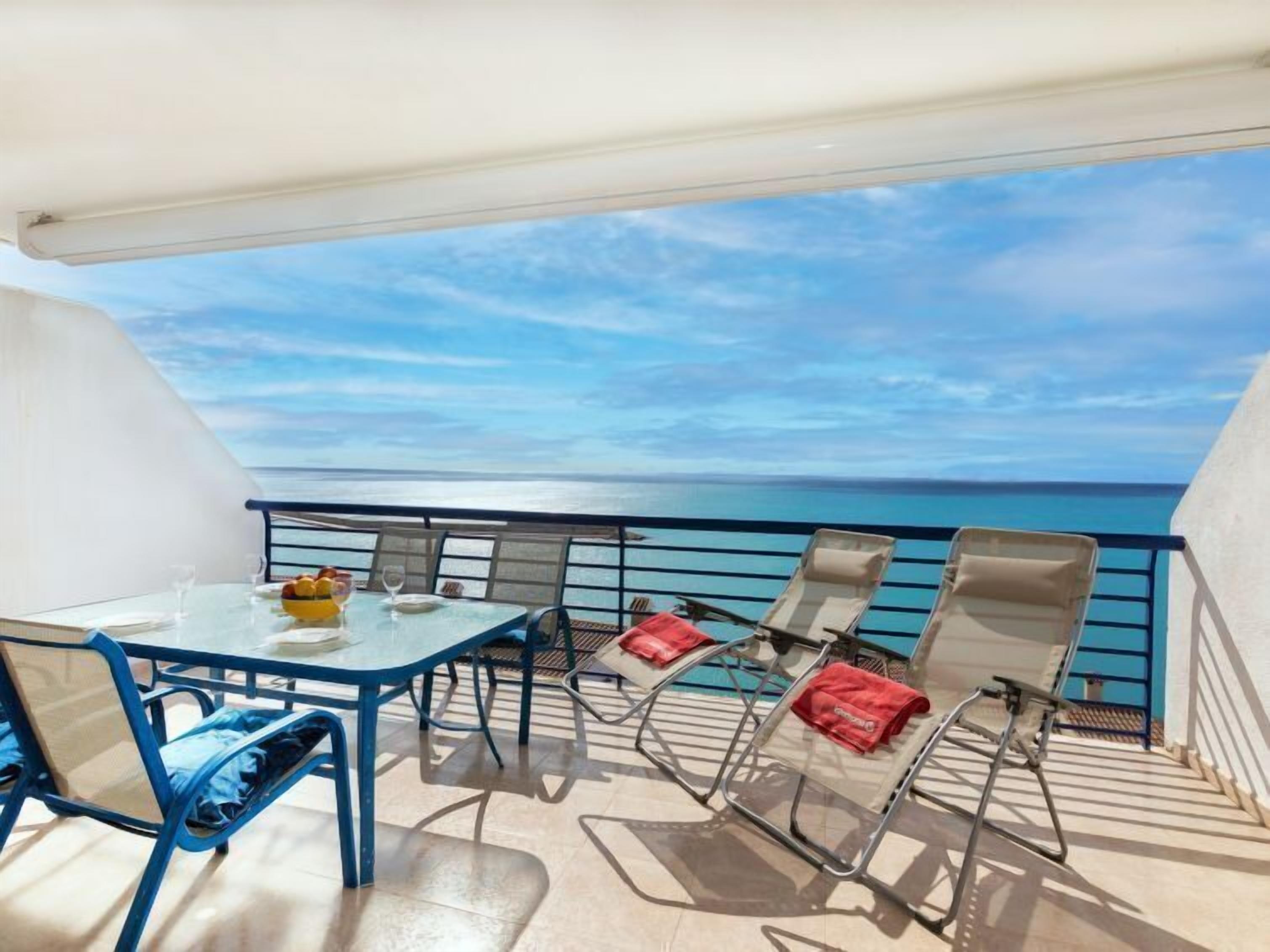 A balcony with a table and chairs, overlooking the sea.
